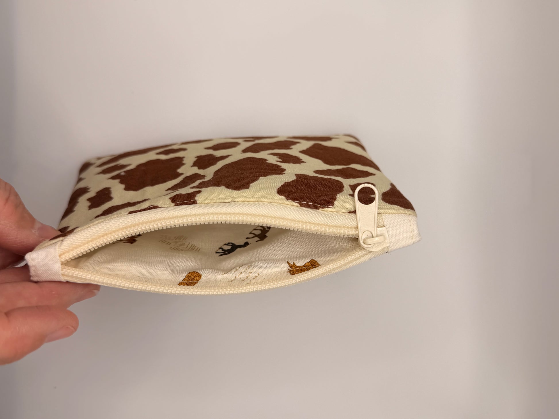 Small pouch with cow print pattern held by a hand against a neutral background